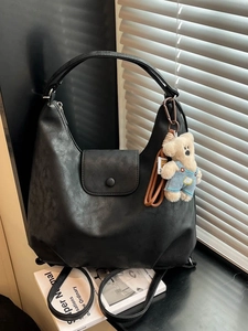 Retro black leather hobo bag with teddy bear charm in natural window light