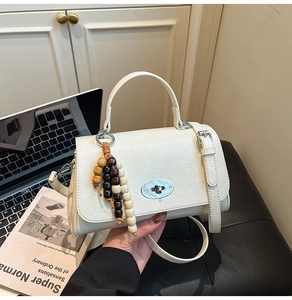 Detail of white vintage crossbody bag featuring silver oval metal lock and wooden beads charm
