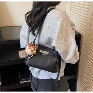 Detail of black pebbled leather handbag featuring a silver turn-lock and cute bear charm