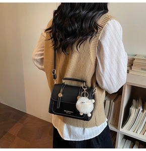 Detail of black leather crossbody bag with white stitching and plush lamb charm