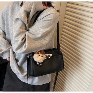 Close-up of black lychee leather shoulder bag with silver buckle and plush bear charm