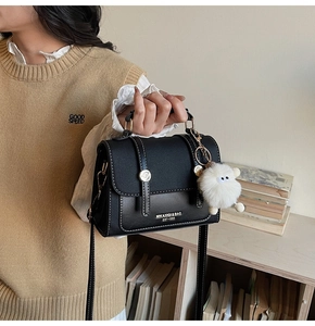 Detail of black leather flap crossbody bag with white stitching and plush sheep charm