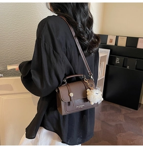 Detailed side view of dark brown vintage leather crossbody bag with white plush charm
