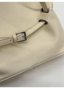 Detail view of cream tote bag featuring matte leather texture and silver buckle strap
