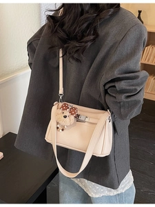 Minimalist beige crossbody bag with plush bear charm worn by model in casual style