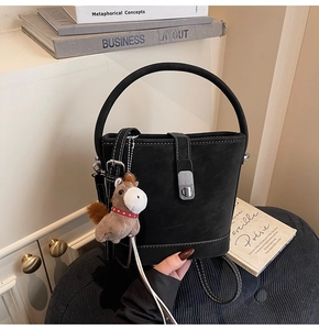 Détail du sac seau en daim noir avec coutures blanches et un charm de cheval marron
