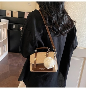 Detail view of a vintage beige canvas and brown leather crossbody bag with a fur ball charm