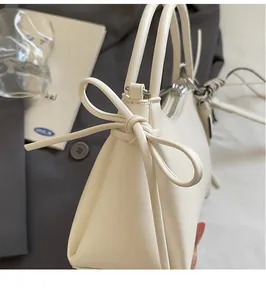 Detalle de elegante bolso de cuero crema con lazo decorativo lateral y textura refinada