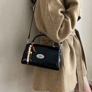 Detail view of black glossy leather handbag with silver turn-lock and beaded charm