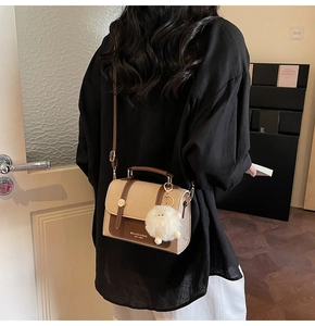 Detail view of stylish beige fabric and brown leather crossbody bag with fluffy charm