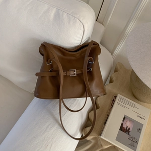 Detail view of brown vintage leather tote with silver metal buckle on a white sofa