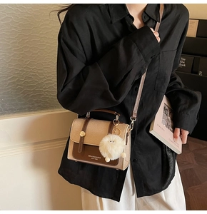 Close-up of retro beige and brown PU leather crossbody bag with soft white fur pompom charm