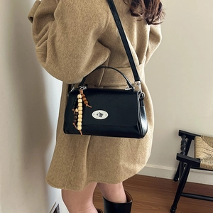 Detail view of black vintage leather crossbody bag with wooden bead charm on a camel coat
