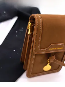 Detail of caramel leather crossbody bag with white stitching and fashion gold lettering