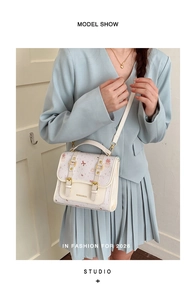 Detail of cream white leather handbag featuring pink bear prints and golden metal buckles