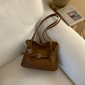 Close-up of caramel brown leather tote bag with silver buckle on a white sofa