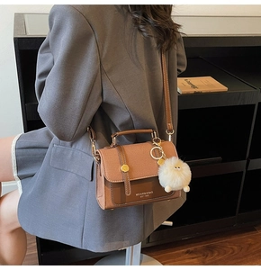 Brown leather crossbody bag with flap and white plush charm worn by model in a chic setting