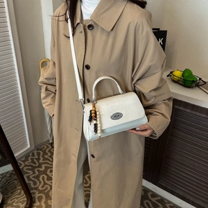 Close-up of white leather handbag with metal turn-lock and wood bead charm detail