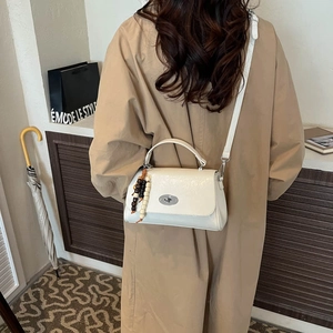 Detailed view of a cream leather handbag with a vintage bead charm worn with a trench coat