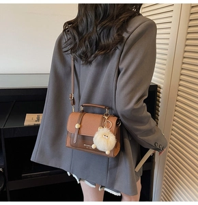 Brown vintage-style small crossbody bag with metal buckles and white plush pendant detail