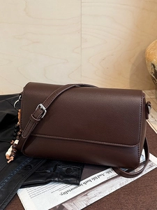 Borsa a tracolla in pelle marrone scuro con ciondolo in legno su sfondo di legno