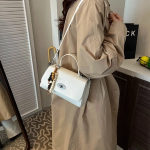 Detail of cream structured handbag featuring a metal twist lock and wooden bead charm