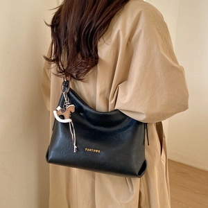 Detail of a large black soft leather tote bag with a golden logo and a horse charm