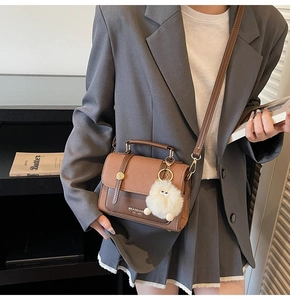 Detail view of a vintage brown crossbody bag with a plush pompom and top handle