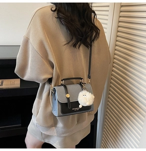 Detail of grey and black color-block crossbody bag with white fur ball and logo lettering