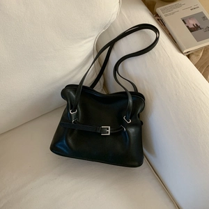 Detailed macro view of black pleated leather tote bag with silver metal buckle on sofa