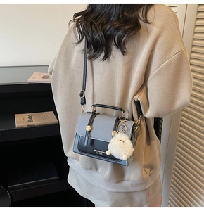 Detail of color-block crossbody bag with grey canvas, black leather, and plush ball charm