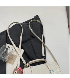 Flat lay of ivory leather backpack with long strap, silver buckle, and teddy bear charm