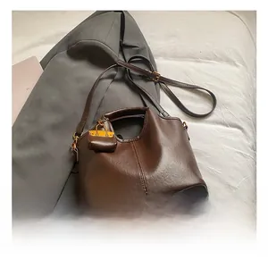 Détail d'un sac à main en cuir marron avec mini breloque et boucle dorée sur un blazer