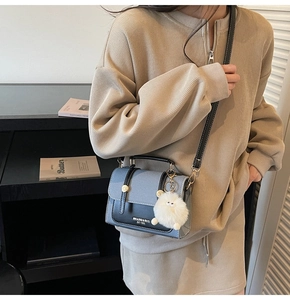 Detail of blue-gray and black crossbody bag featuring gold hardware and a white fur charm