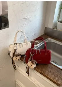 Détail de sacs Boston rétro en crème et rouge avec breloques ours en peluche et chaînes