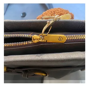 Nahaufnahme von goldenem Metall-Reißverschluss und Logo-Beschlägen an brauner Ledertasche