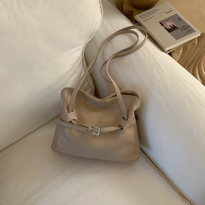Detail of oat beige pleated leather shoulder bag with buckle strap on a soft sofa