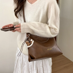 Detail of dark brown tote bag with PANTOVR logo and pony charm on white sweater background
