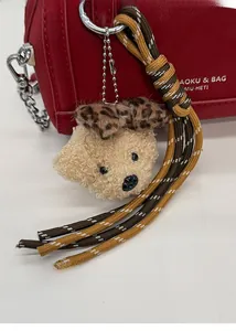 Détail d'un porte-clés ours en peluche avec nœud léopard sur un sac en cuir rouge