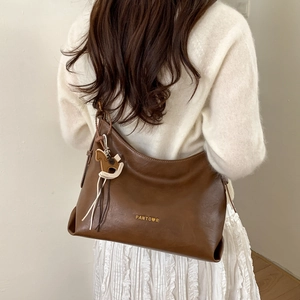 Detail of a large brown leather hobo bag with horse charm and golden logo on a model