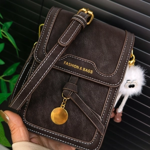 Close-up of brown pebbled leather phone bag with white stitching and plush charm accessory