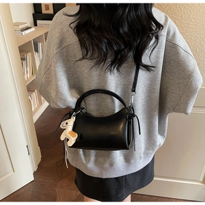 Detail of minimalist black leather crossbody bag with a cute white horse charm accessory