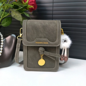 Detail of grey-green crossbody phone bag with contrast stitching and plush doll pendant