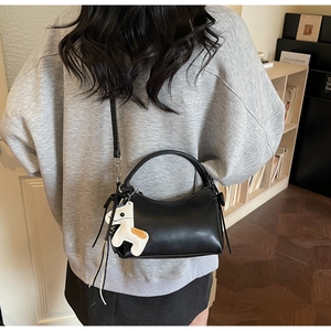 Detail of black matte leather handbag with white horse charm in a warm studio setting