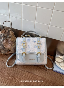 Detail of light blue preppy backpack with golden buckles and romantic cartoon patterns