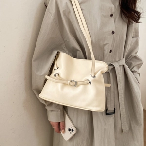 Close-up of beige leather tote bag with decorative metal buckle and dual slim straps