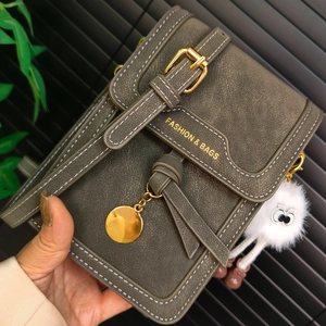 Detail of olive green pebbled leather phone bag with white stitching and plush charm