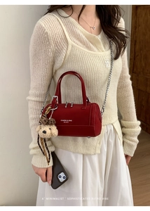 Détail du sac Boston cylindrique rouge avec bandoulière chaîne et breloque ours en peluche