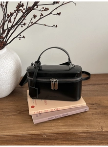 Detail of glossy black box handbag with top handle and metal zipper on art books