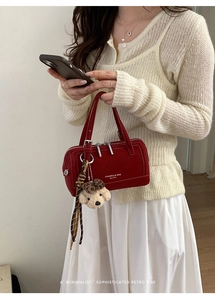 Détail du sac Boston rouge en cuir avec fermeture éclair et breloque ours en peluche